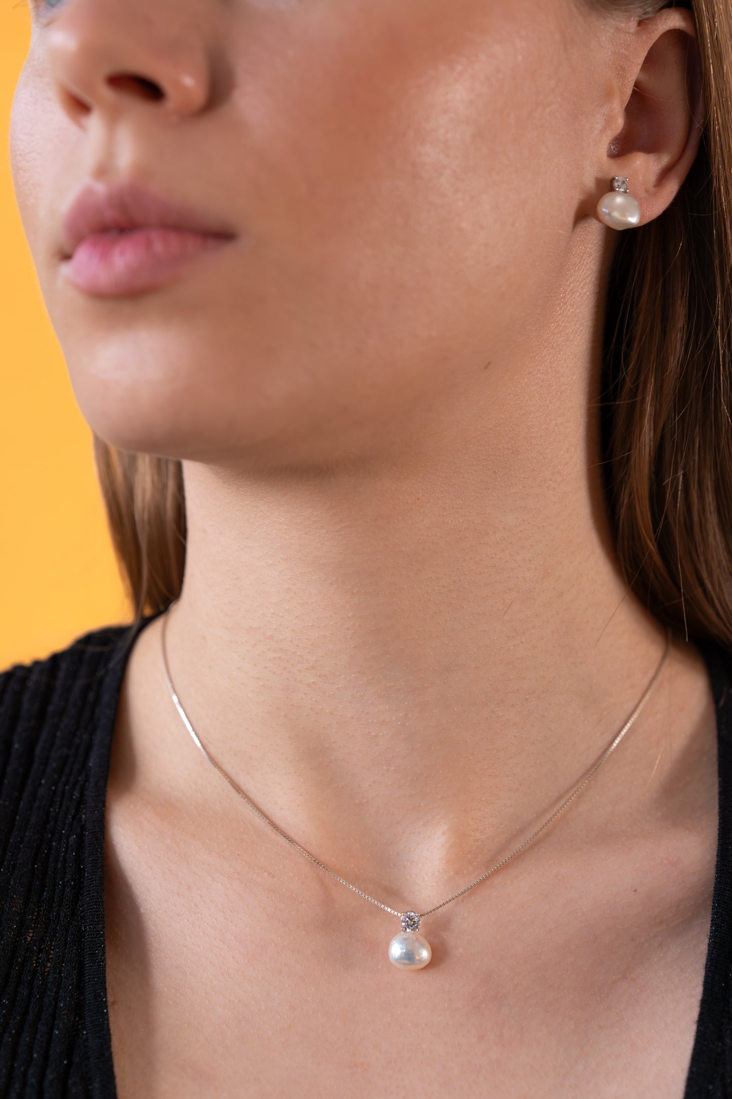 Close-up of a woman wearing a pearl necklace and earrings against an orange background