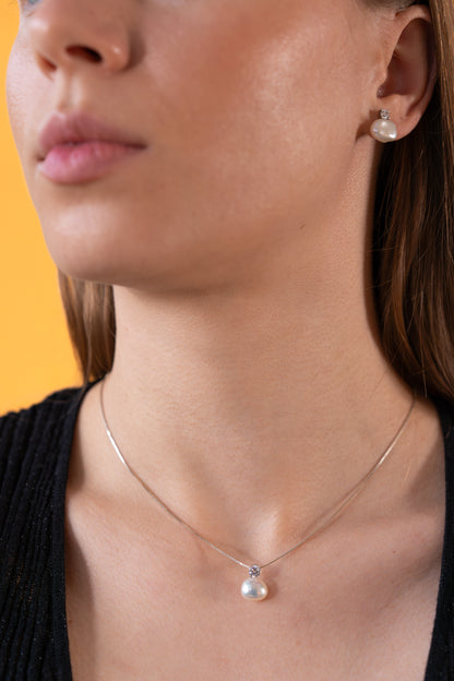 Close-up of a woman wearing a pearl necklace and earrings against an orange background