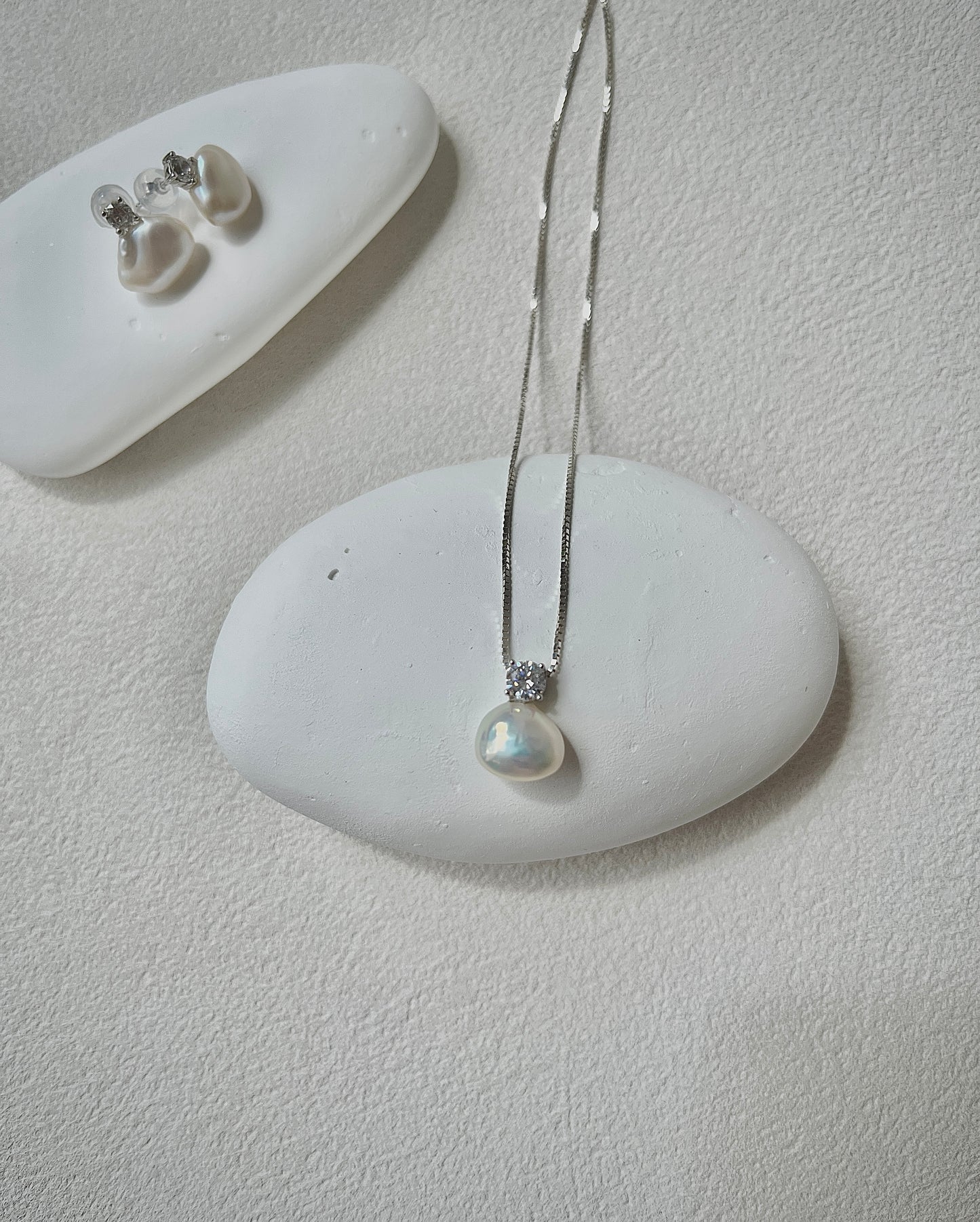 Pearl necklace and earrings on a white stone surface