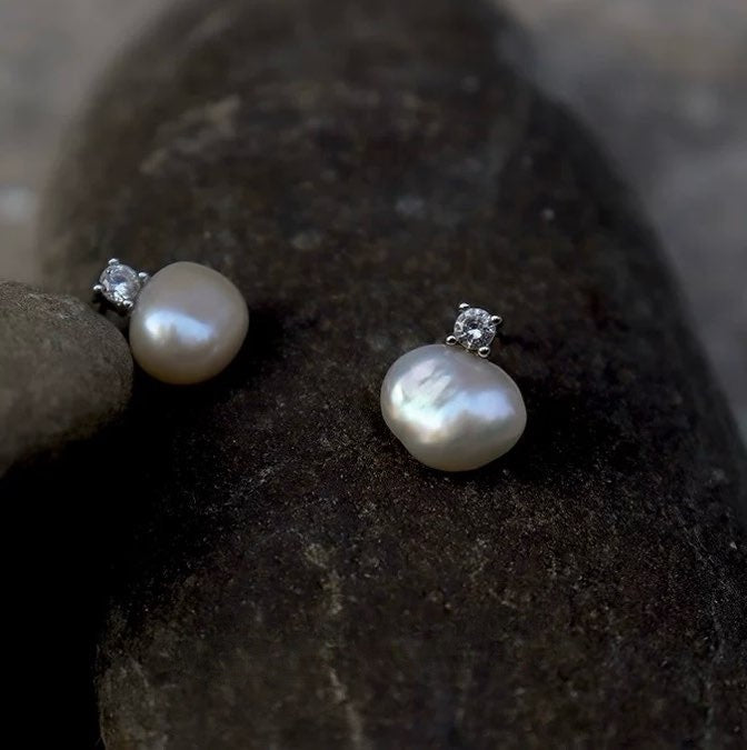 Pearl earrings with silver settings on a dark stone surface