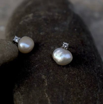 Pearl earrings with silver settings on a dark stone surface
