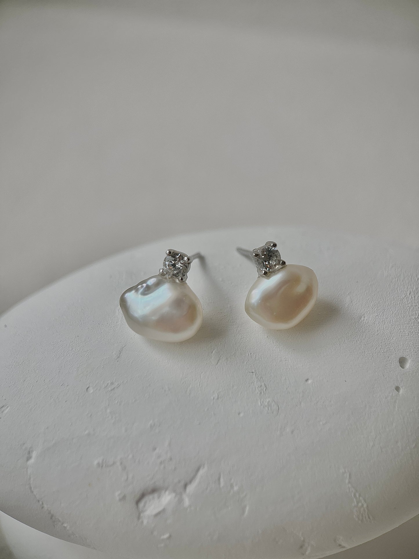 Pearl earrings with silver accents on a textured white surface