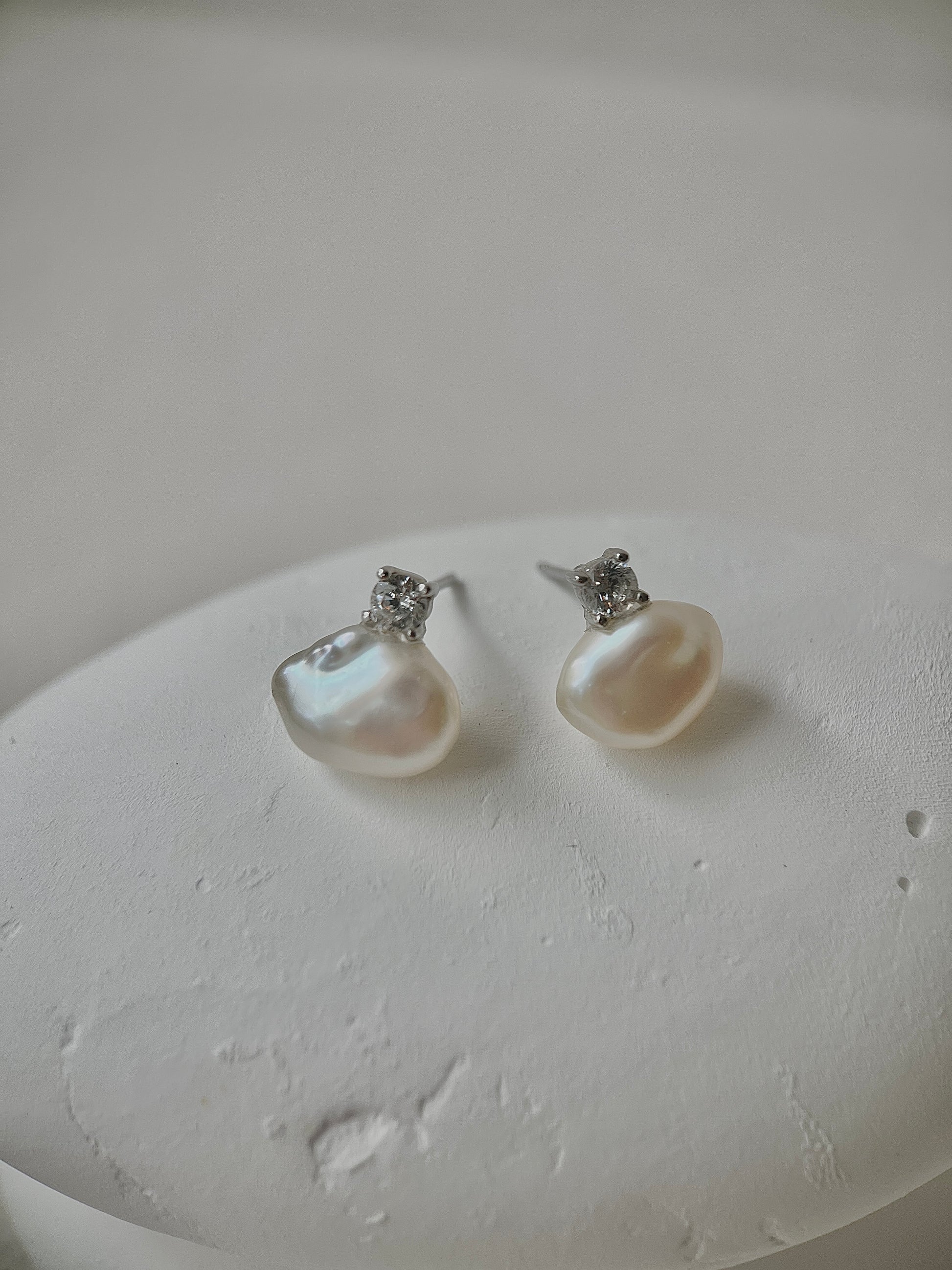Pearl earrings with silver accents on a textured white surface