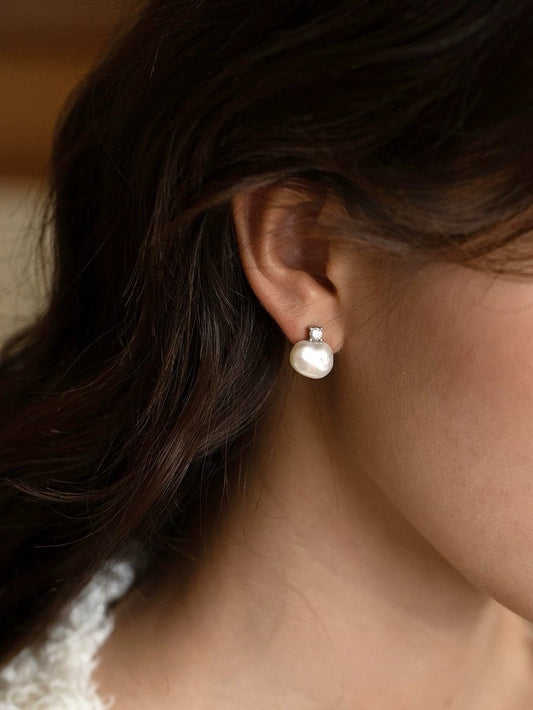 Close-up of an ear wearing a pearl earring with dark hair and lace fabric in the background