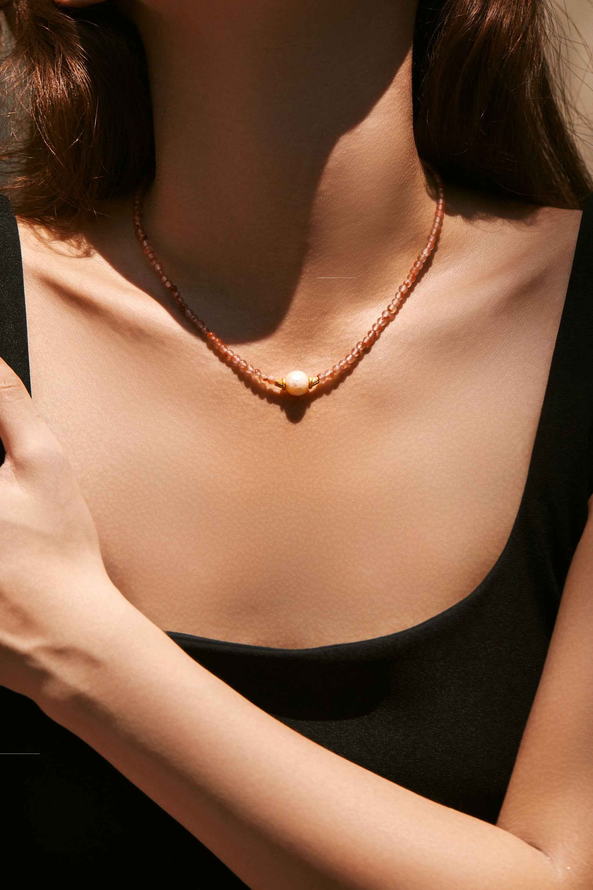 Close-up of a person wearing a red carnelian pearl necklace with a black top.