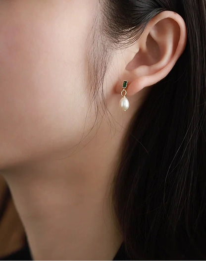 Close-up of an ear wearing a pearl earring with a dark gemstone.