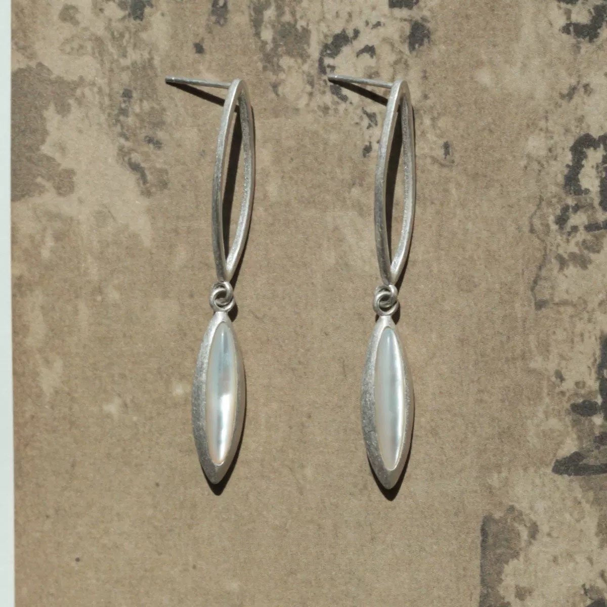 Pair of silver earrings on a textured beige background