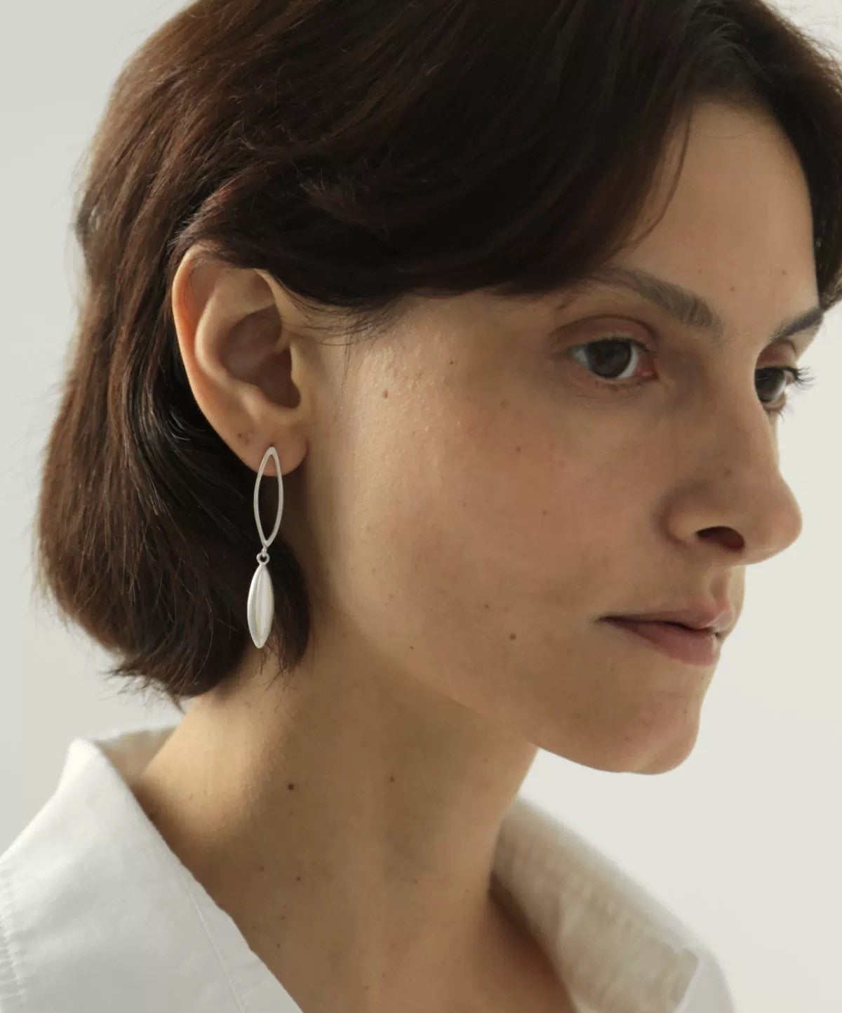 Close-up of a woman wearing silver earrings with a plain background