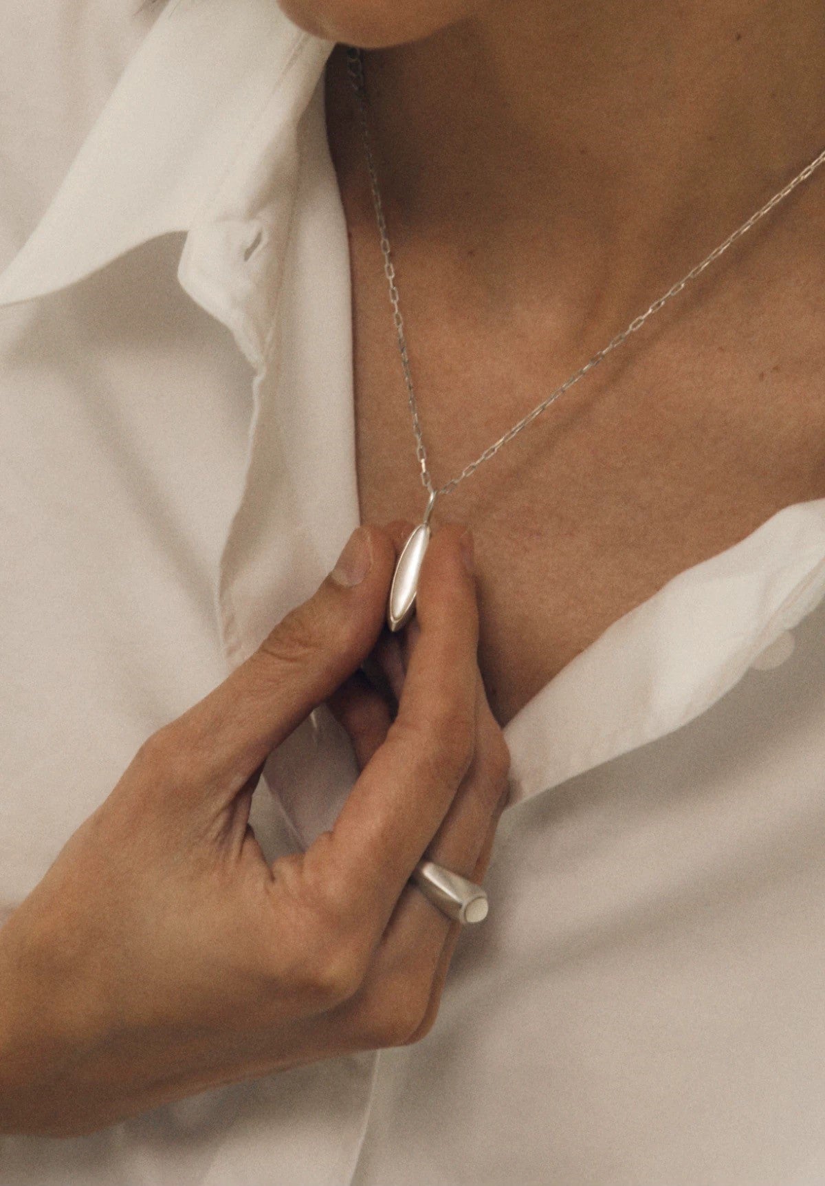 Person adjusting a silver nacre necklace with a plain background