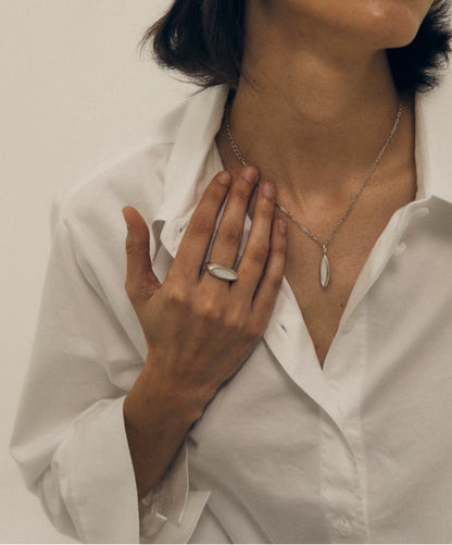 Person wearing a nacre necklace and nacre ring with a plain background