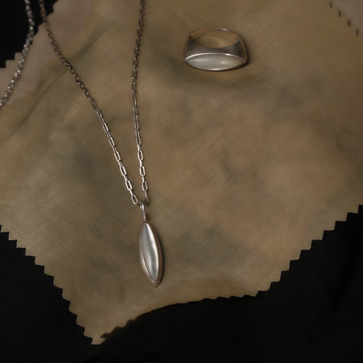 Silver necklace with a nacre pendant and ring on a textured beige surface