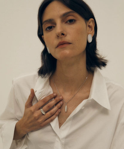 Woman wearing a white shirt with jewelry, including earrings and a silver nacre necklace.