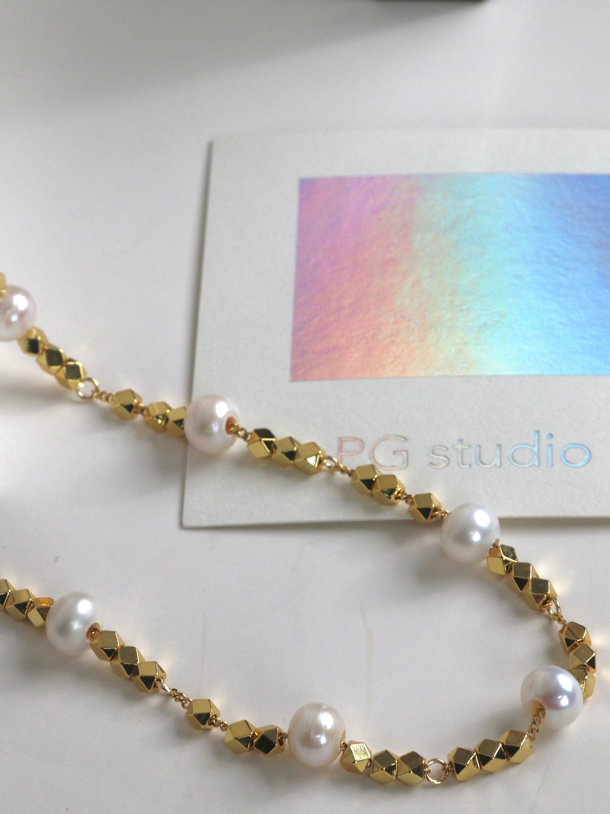 Gold and pearl necklace for men on a white surface with a colorful card in the background