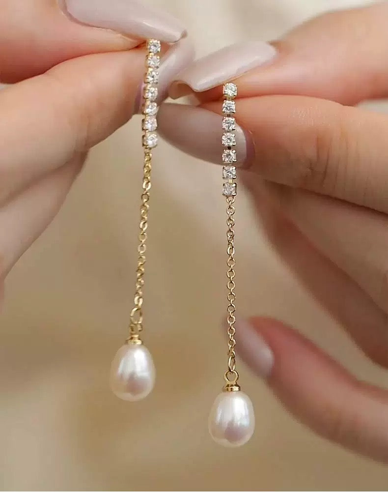 Pearl and gold chain earrings held between fingers against a neutral background