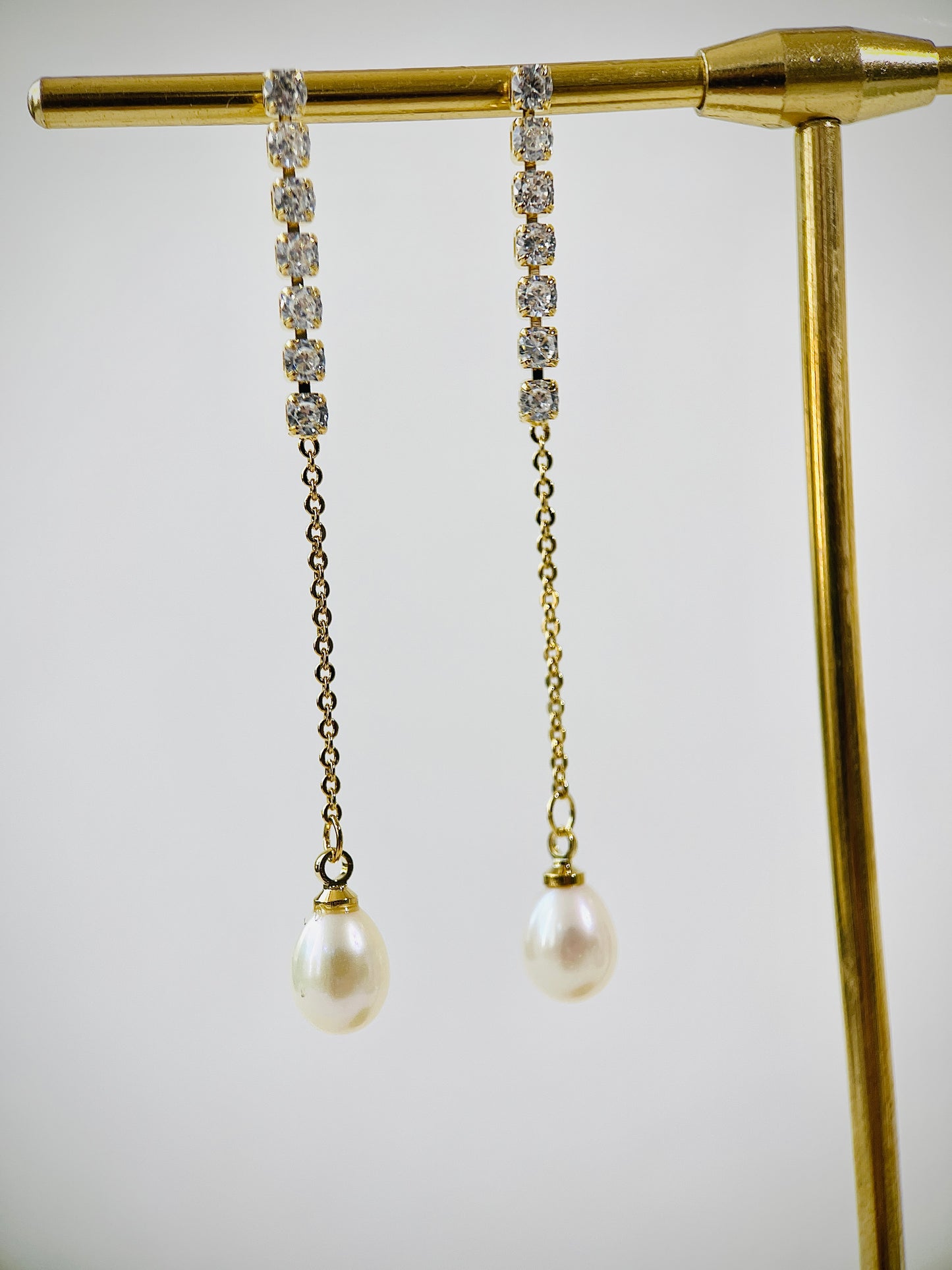 Pearl and crystal drop earrings on a gold stand against a white background