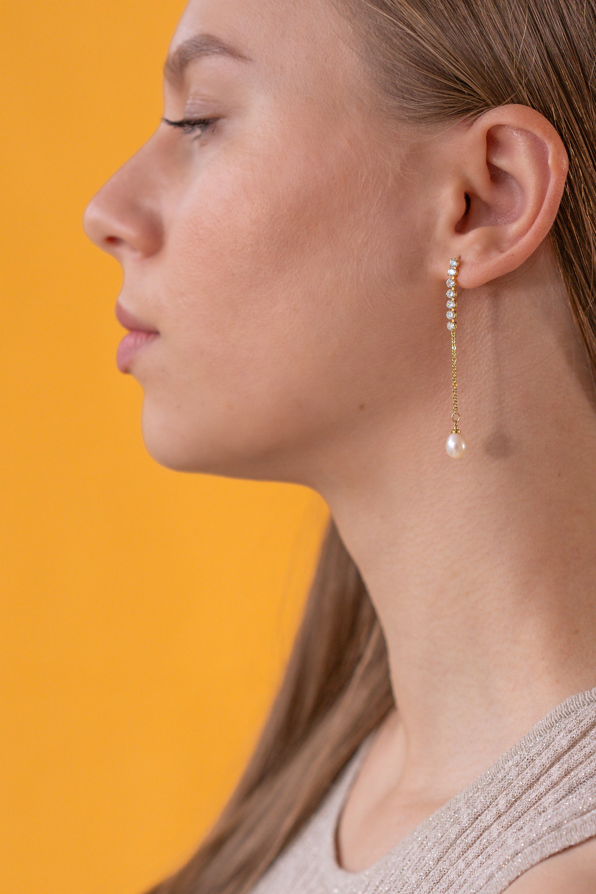 Close-up of a woman wearing a pearl dangling earring against an orange background