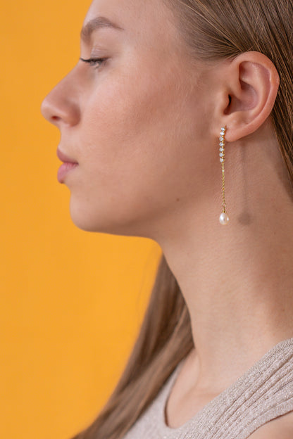 Close-up of a woman wearing a pearl dangling earring against an orange background