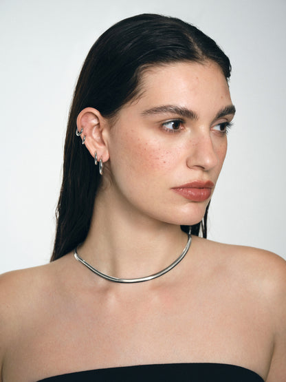 Woman wearing a silver necklace and several Rhodium-plated silver earrings against a plain background
