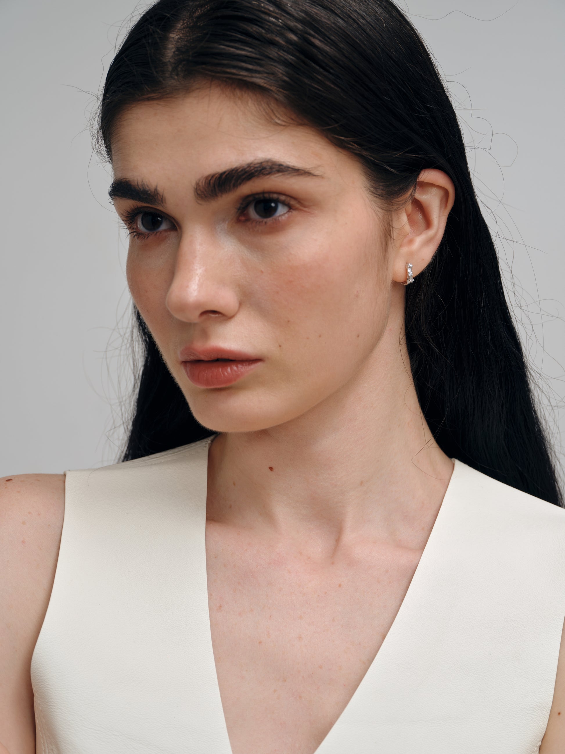 Woman with long dark hair wearing a silver zircon earrings against a plain background