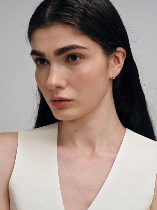 Woman with long dark hair wearing a silver zircon earrings against a plain background