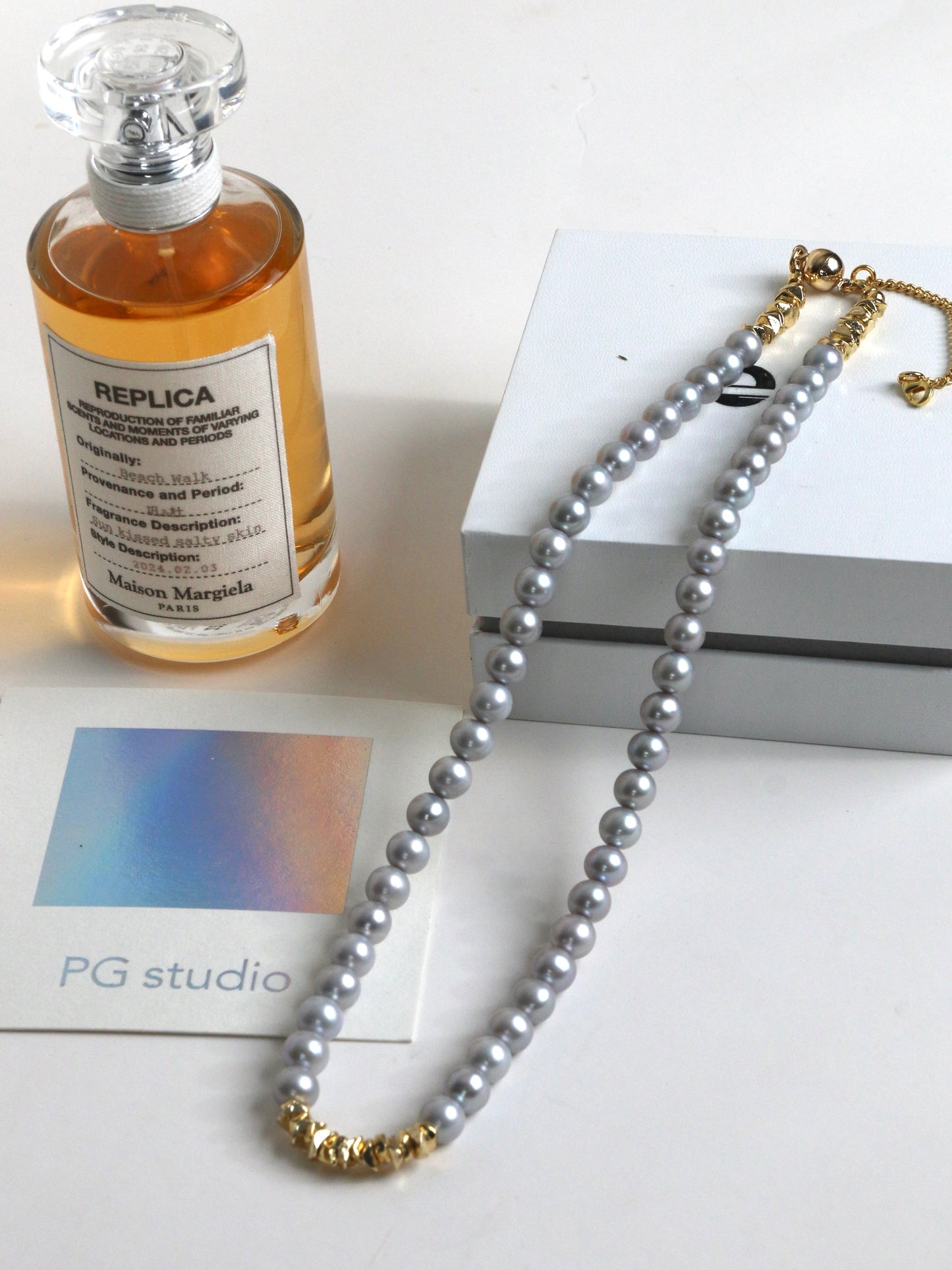 Silver Pearl necklace for men with gold clasp next to a perfume bottle labeled 'Replica' on a white surface.