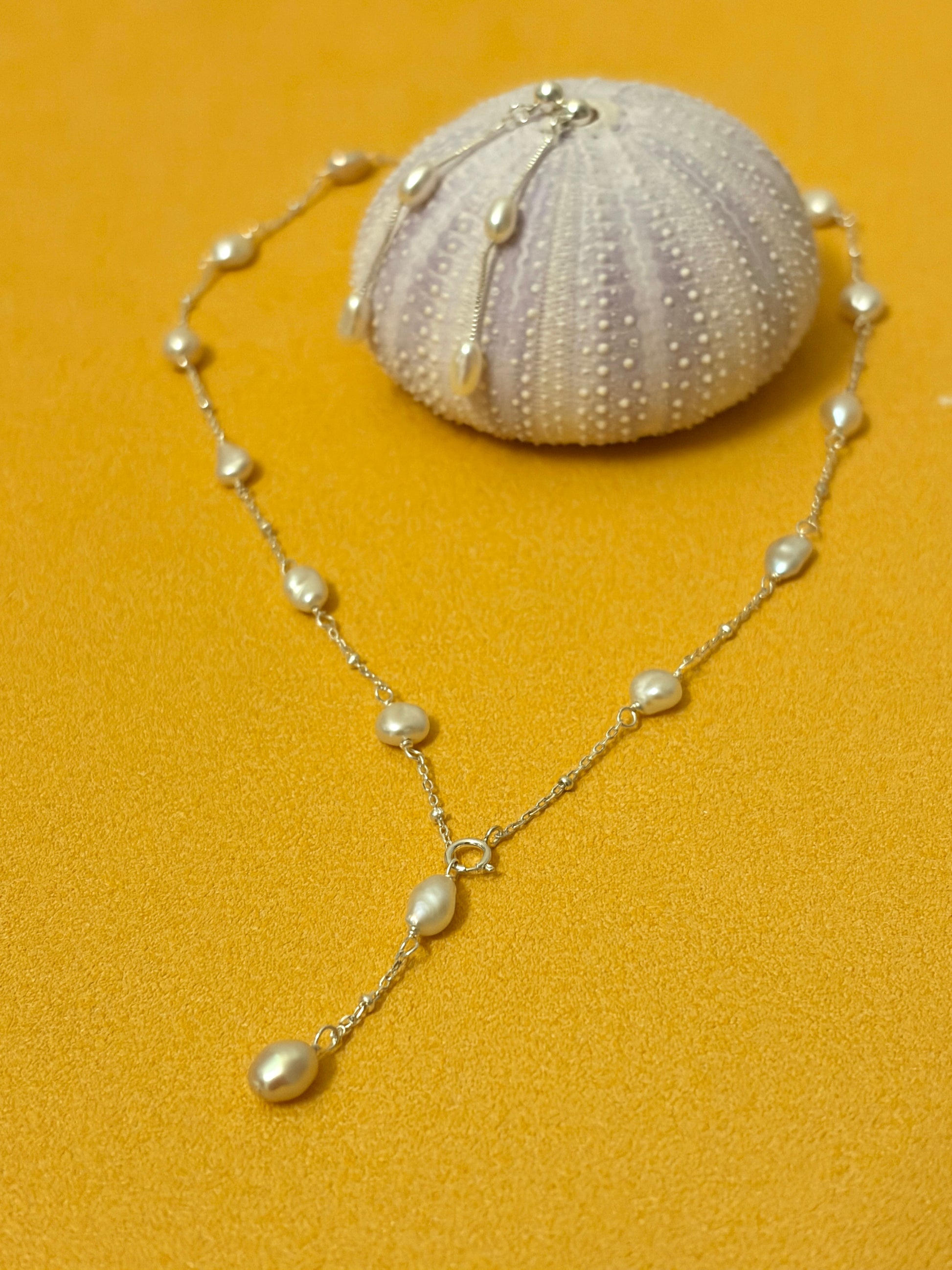 Small Keshi Pearl Necklace displayed on a vibrant orange background with a seashell.