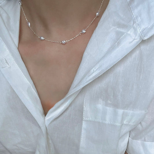Necklace with small pearl pendants on a person wearing a white shirt.