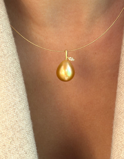 Gold necklace with a teardrop-shaped or pear shaped pearl pendant on a person wearing a beige sweater.
