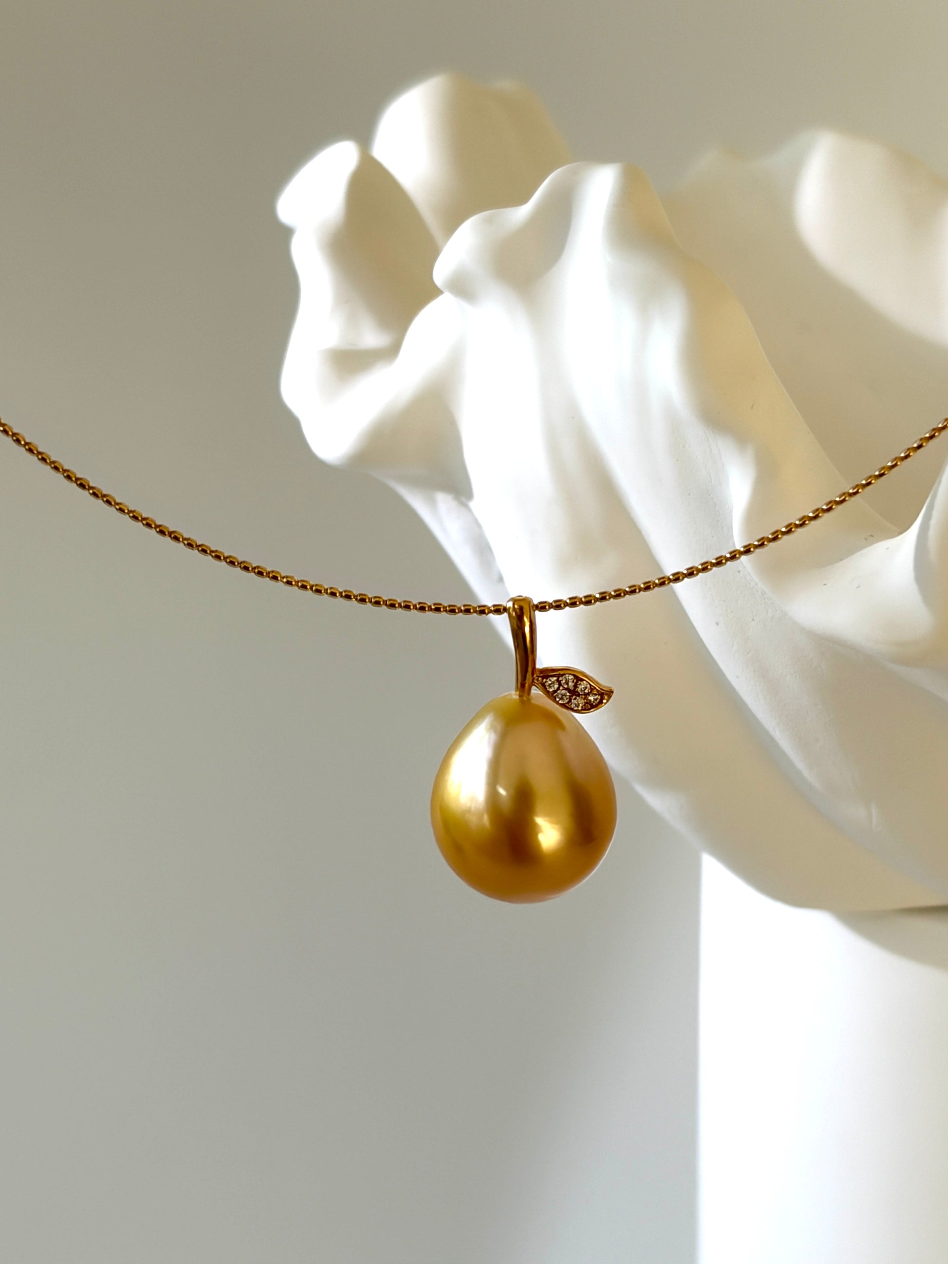 Golden pear shaped pendant on a chain against a white marble sculpture background