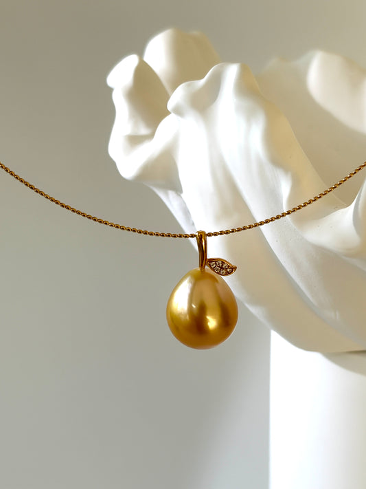 Golden pear shaped pendant on a chain against a white marble sculpture background