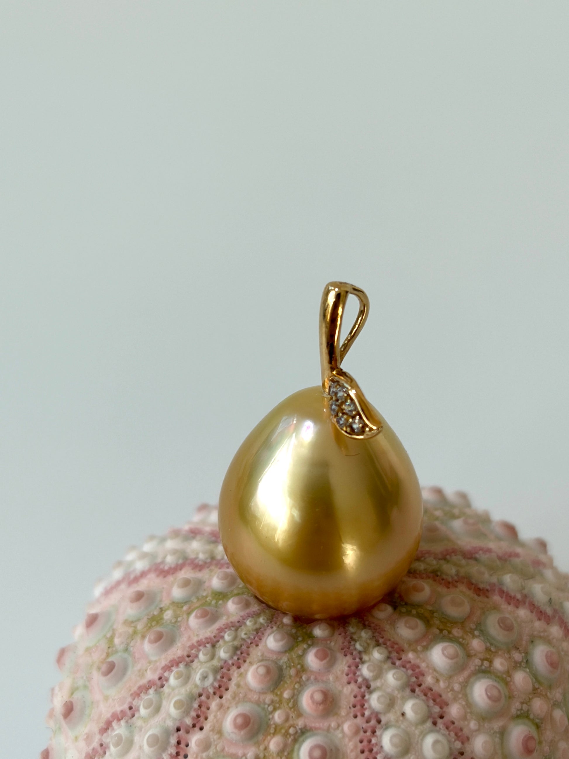 Golden pear shaped pendant with a small diamond on a textured shell background