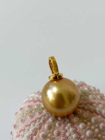 Gold pearl pendant with AU750 mark on a textured surface with a light gray background