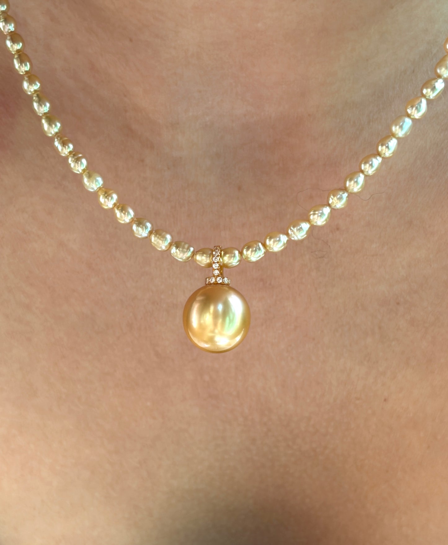 Pearl necklace with a large gold pearl pendant on a person's neck.
