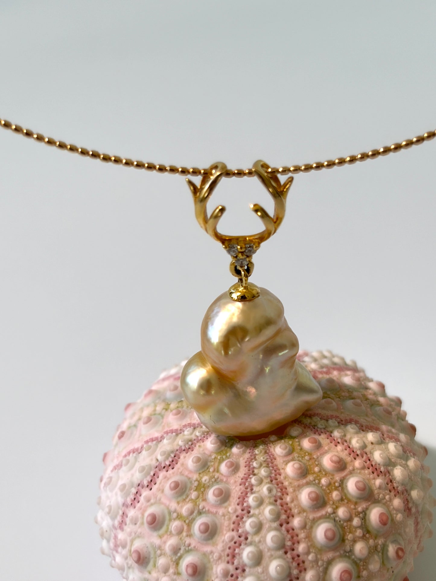 Necklace with a south sea golden keshi pearl pendant on a textured sphere against a light background
