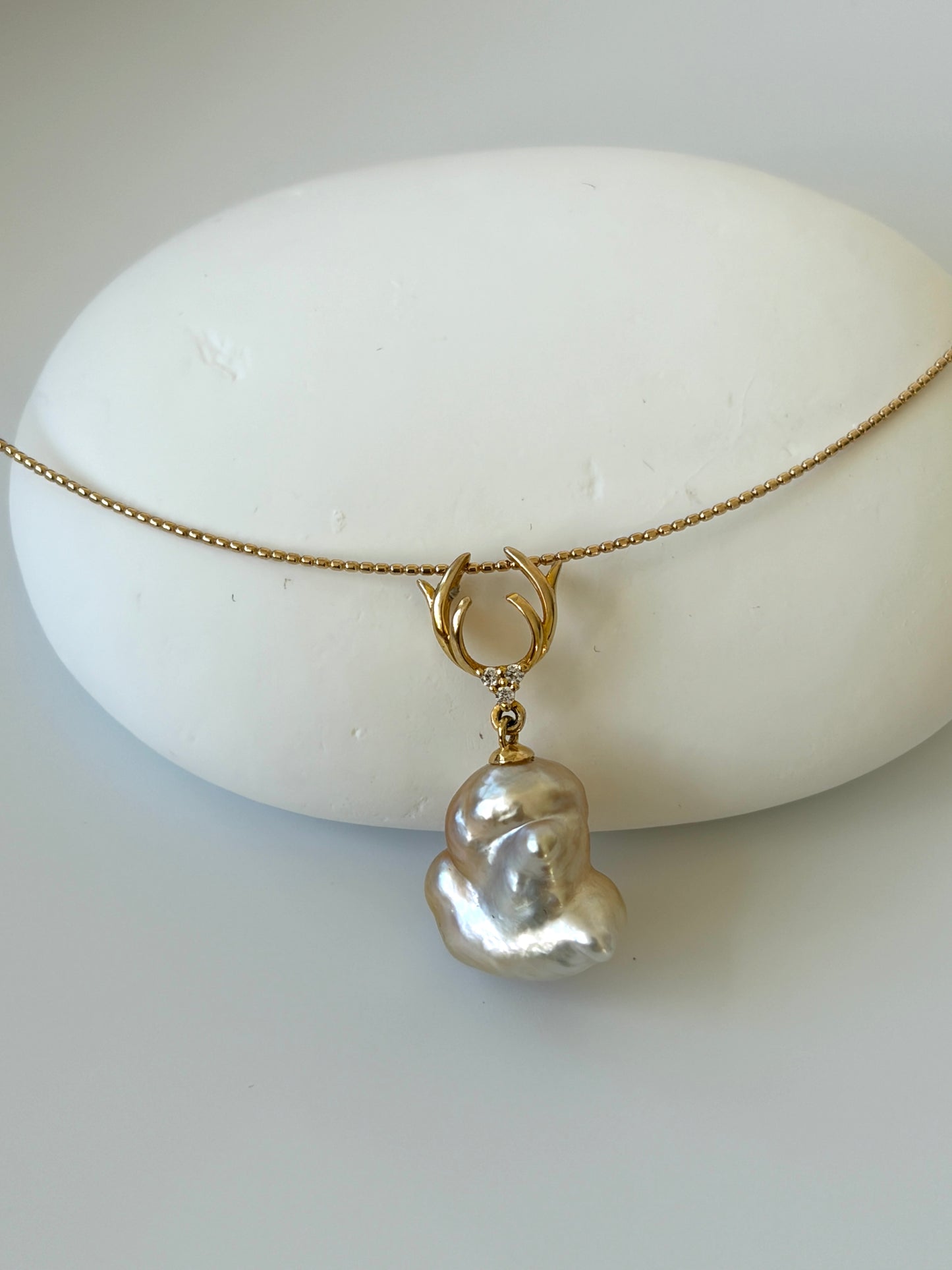 Necklace with a south sea golden keshi pearl pendant on a textured sphere against a light background