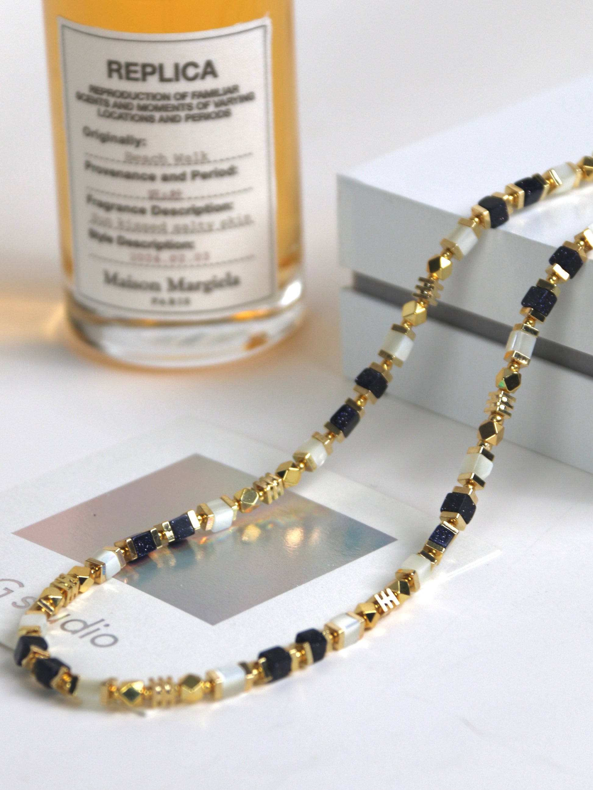 Necklace for men with gold, black, and white agate on a white surface with a perfume bottle in the background.