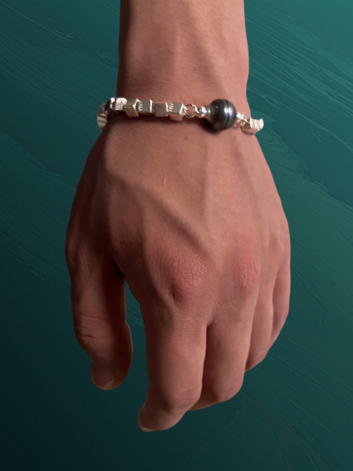 Hand wearing a tahitian pearl silver bracelet on a teal background