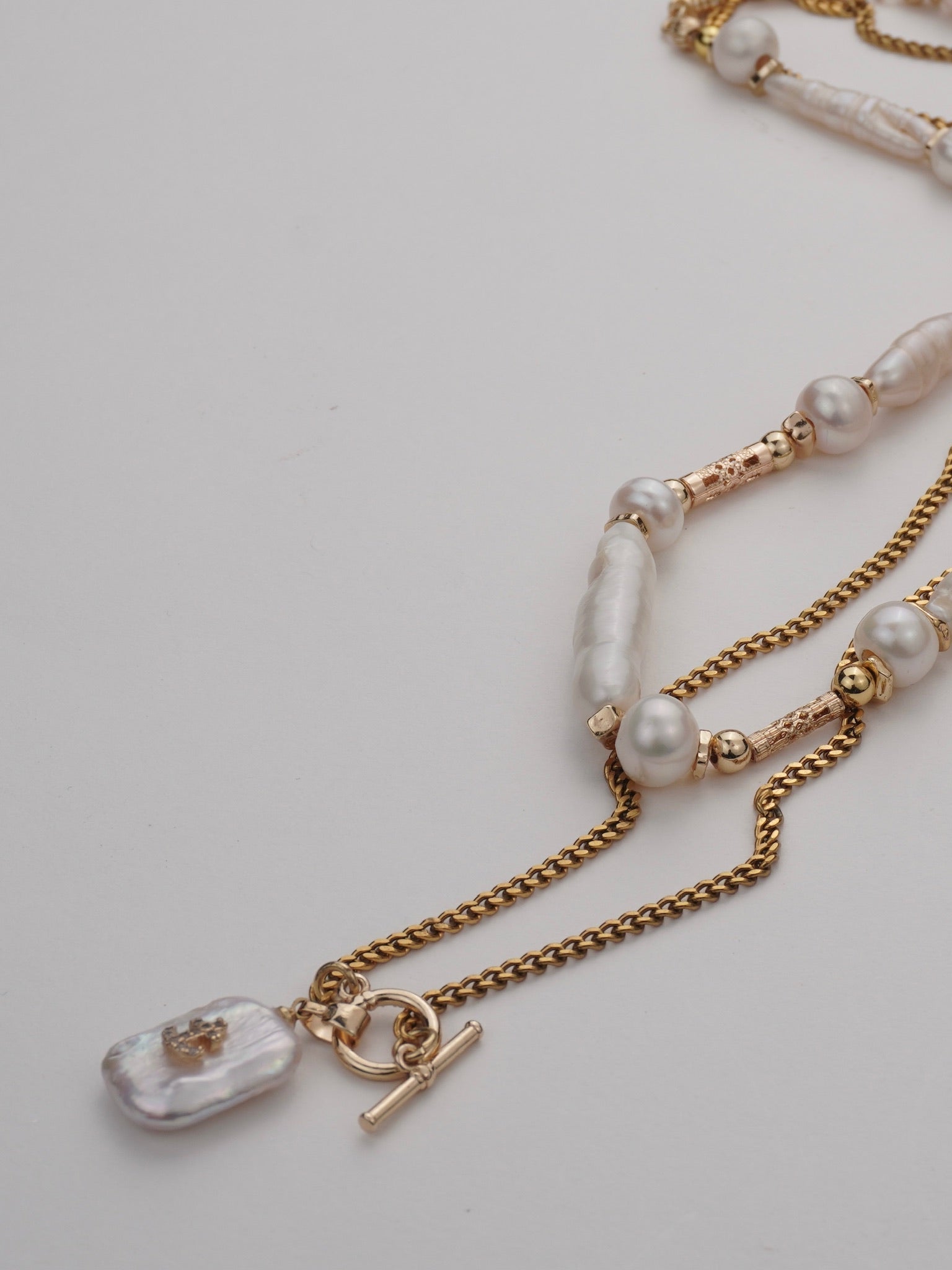 Necklace with gold chain and pearl beads on a light gray background