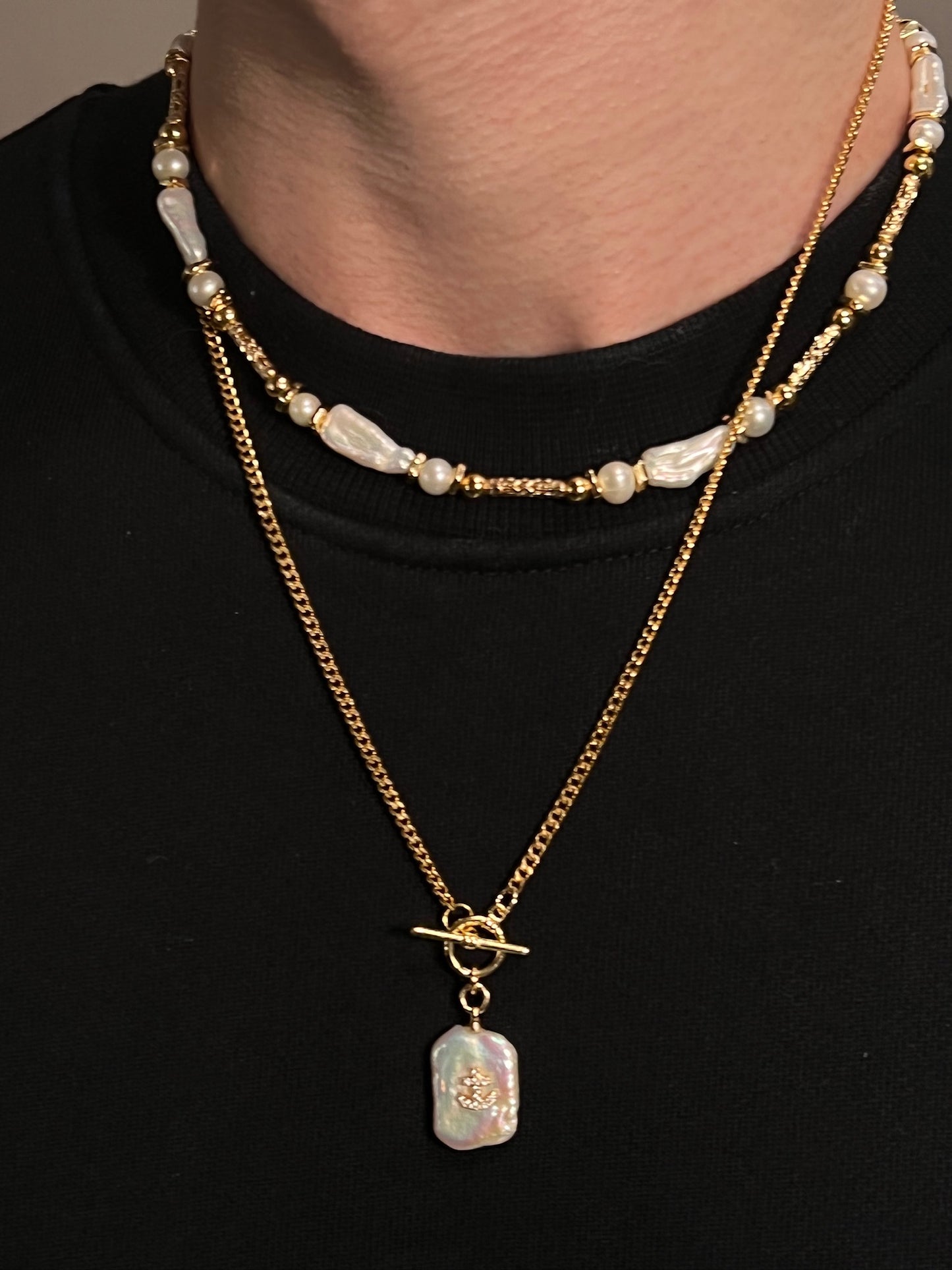 Gold necklace set with pearl accents and a pendant on a black background