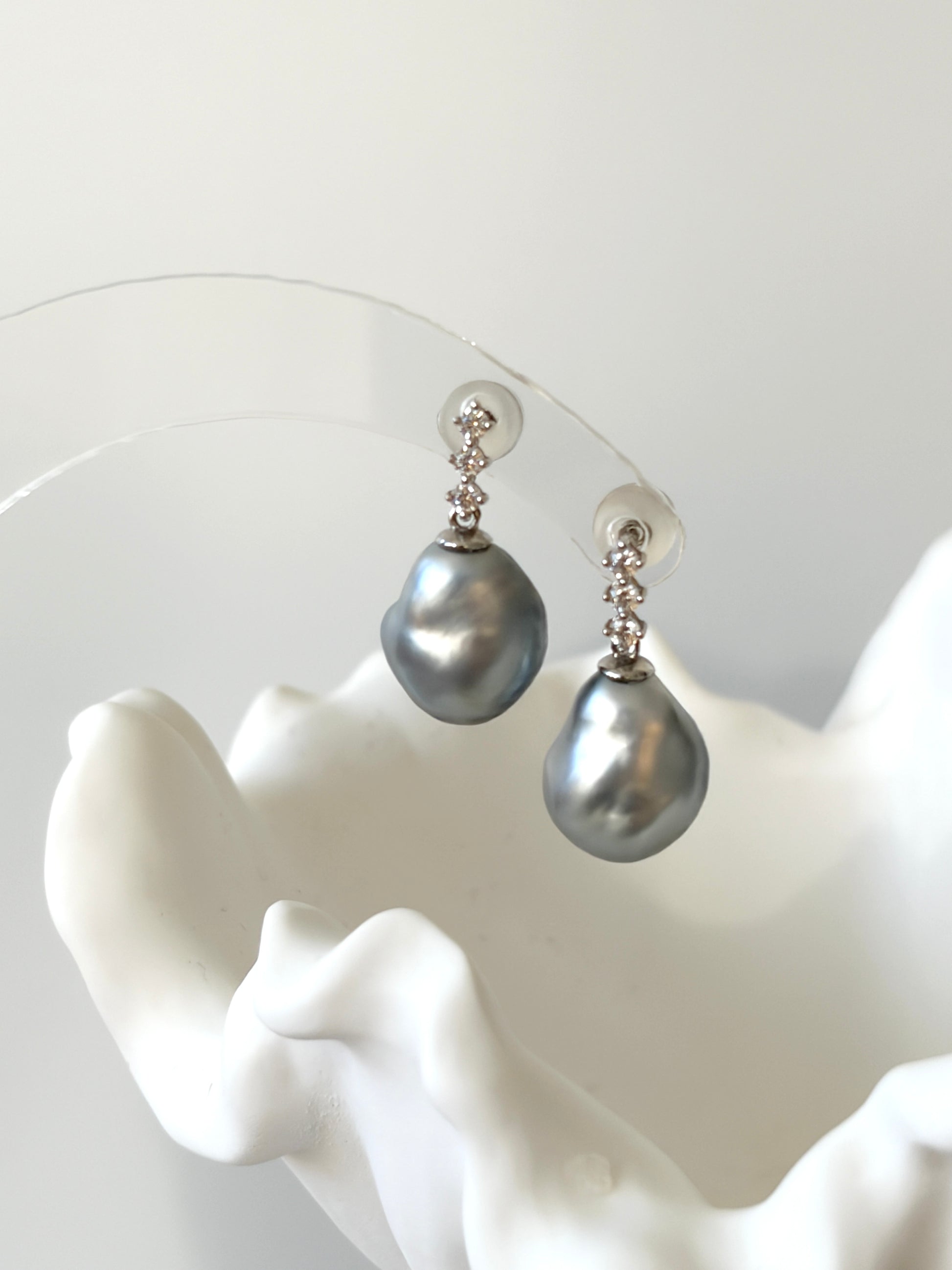 Pair of tahitian keshi pearl earrings with gray pearls on a white mannequin hand.