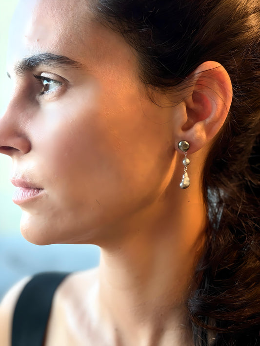 Close-up of a woman wearing Tahitian Keshi pearl earrings with a blurred background