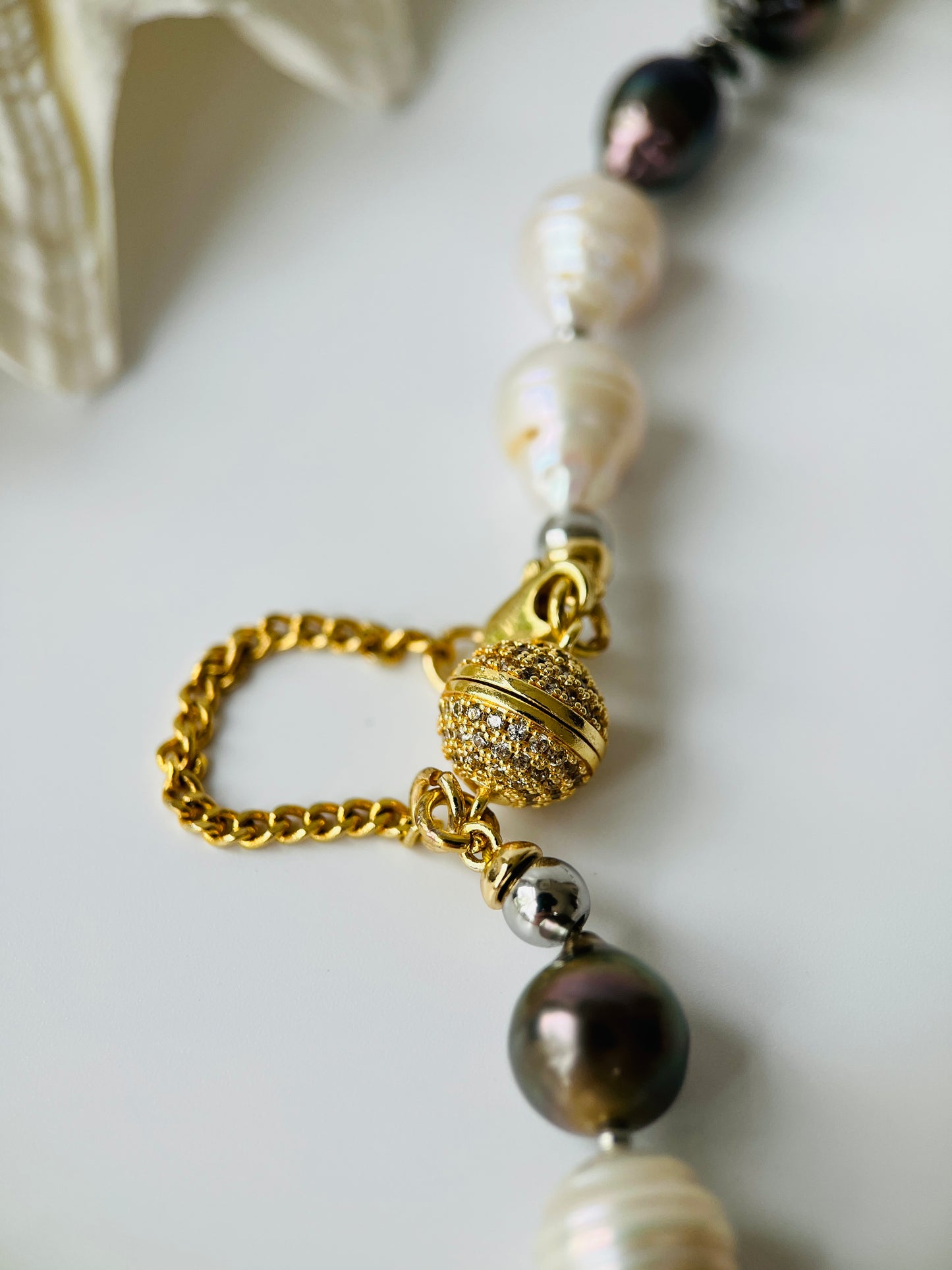 Pearl necklace with a gold clasp and black Tahitian pearls on a light background