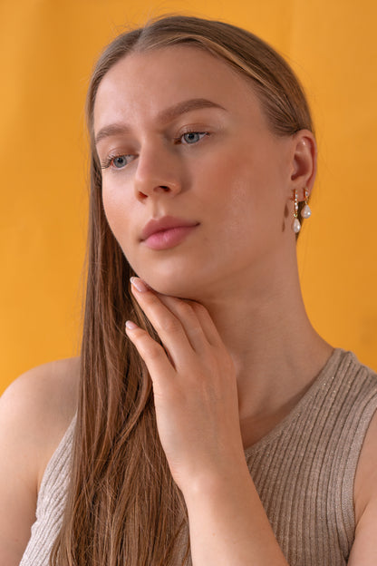 Woman wearing gold baroque pearl earrings against a yellow background