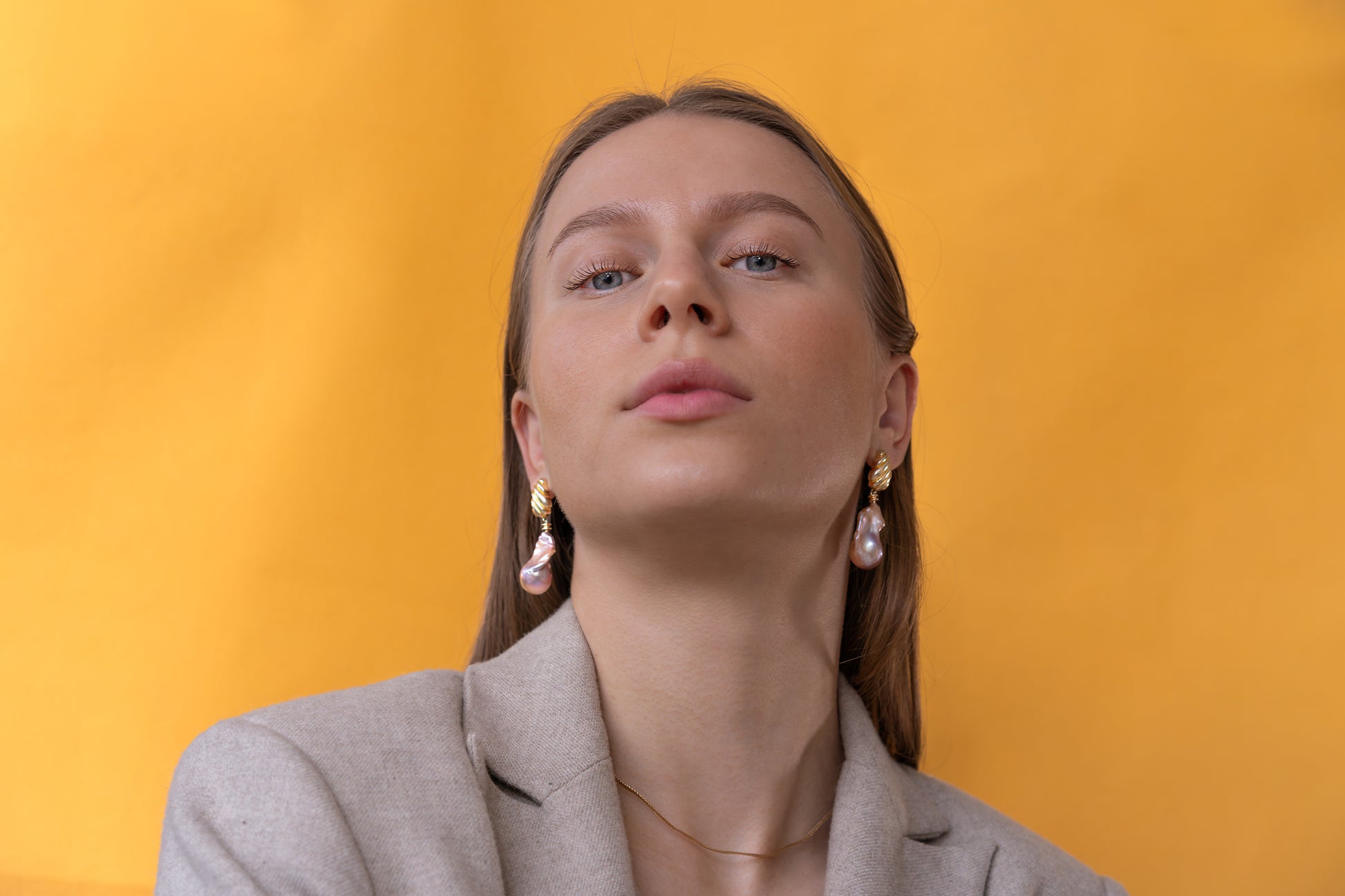 Woman wearing large baroque earrings against a yellow background