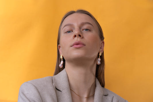 Woman wearing large baroque earrings against a yellow background