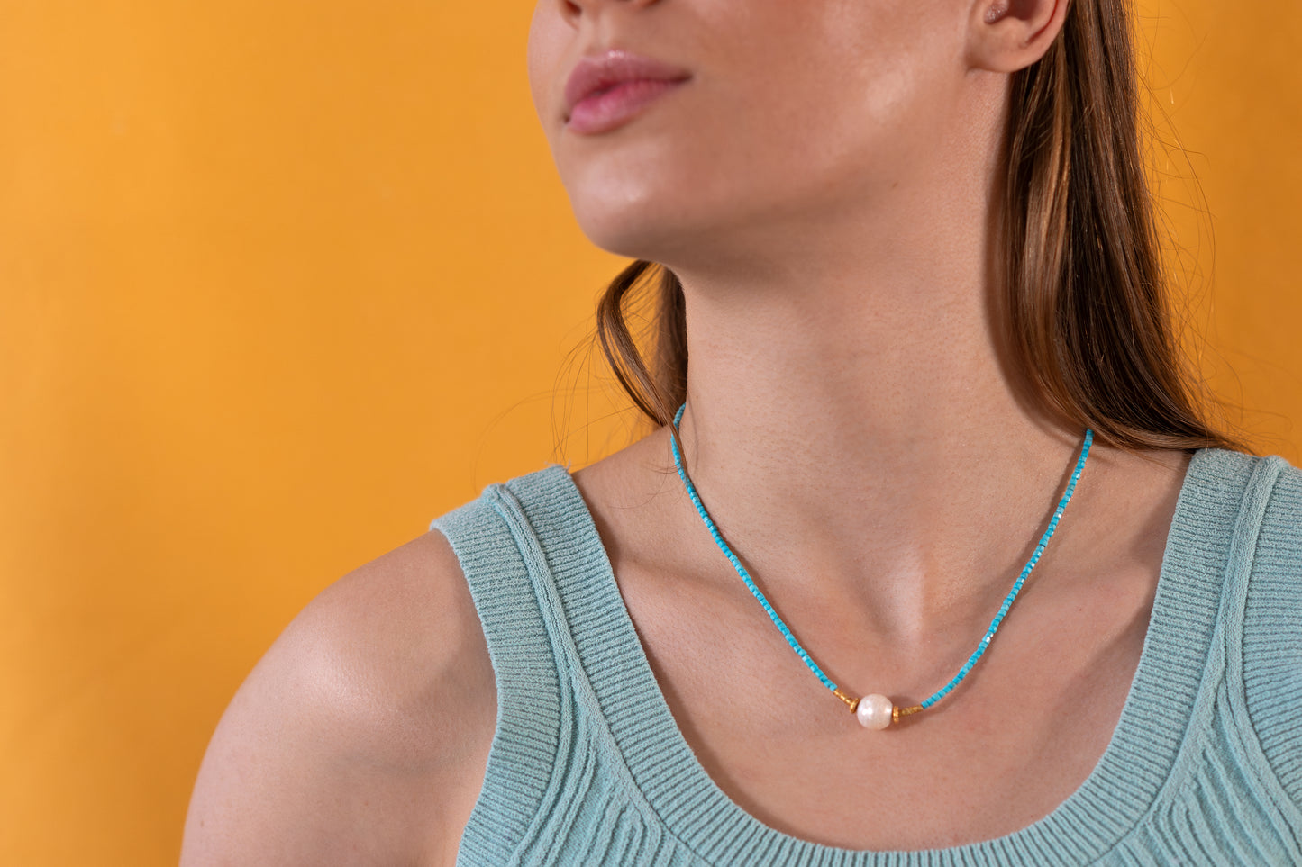 Woman wearing a blue beaded Turquoise necklace against an orange background