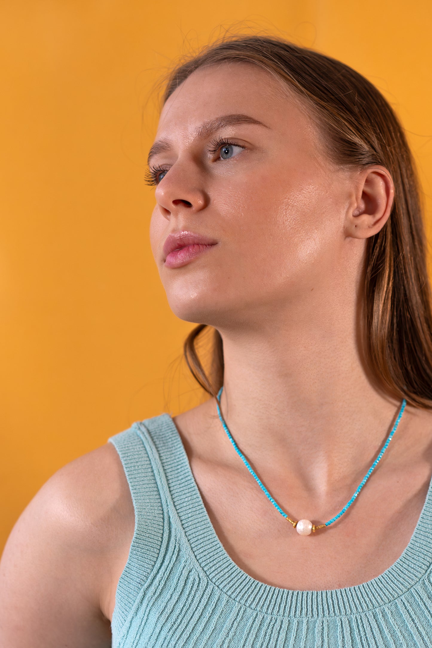 Woman wearing a light blue tank top and a Turquoise necklace against an orange background