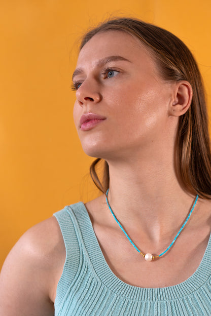 Woman wearing a light blue tank top and a Turquoise necklace against an orange background