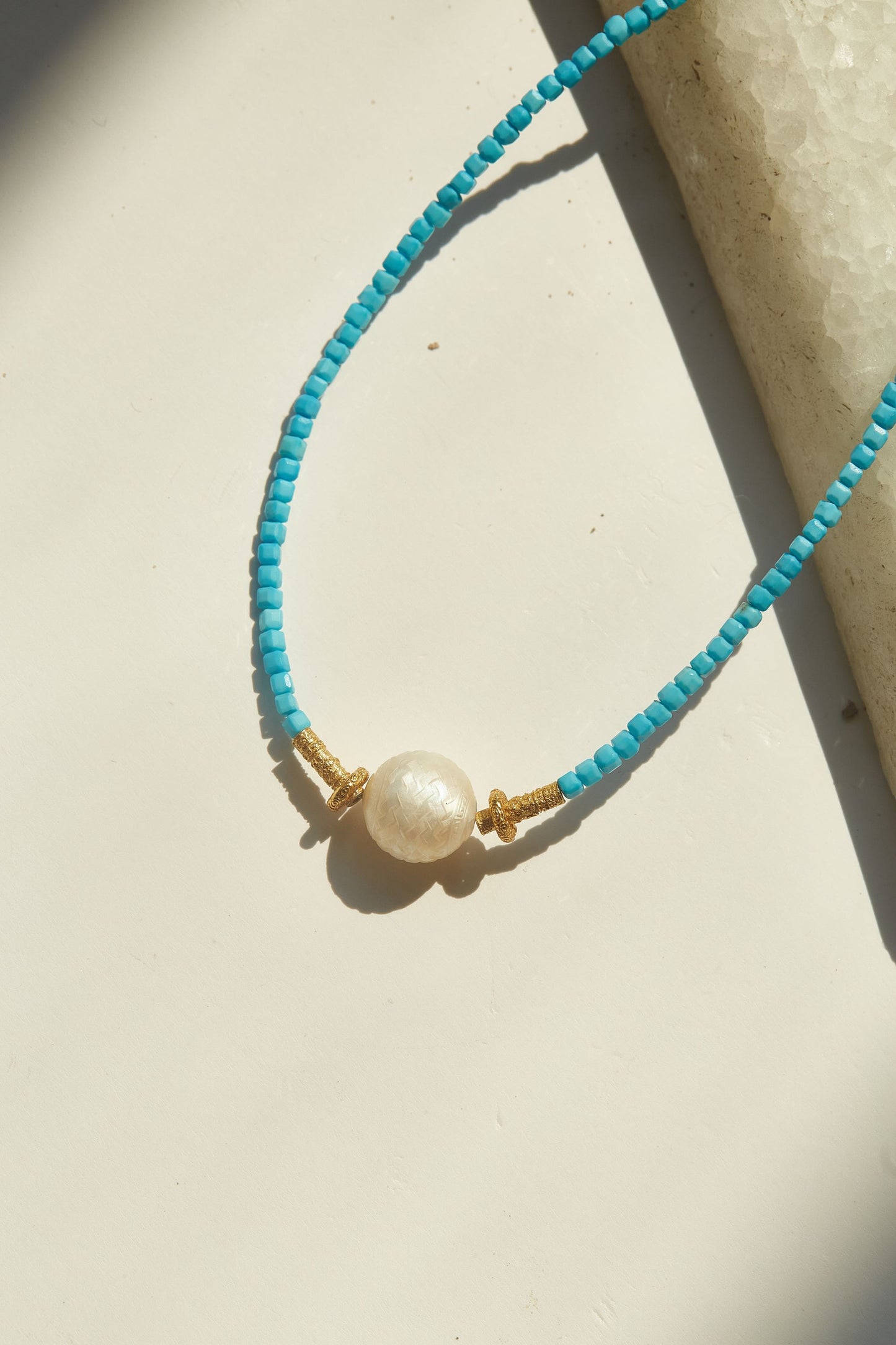 Turquoise beaded necklace with a pearl pendant on a beige surface