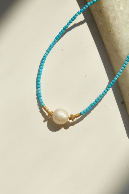 Turquoise beaded necklace with a pearl pendant on a beige surface